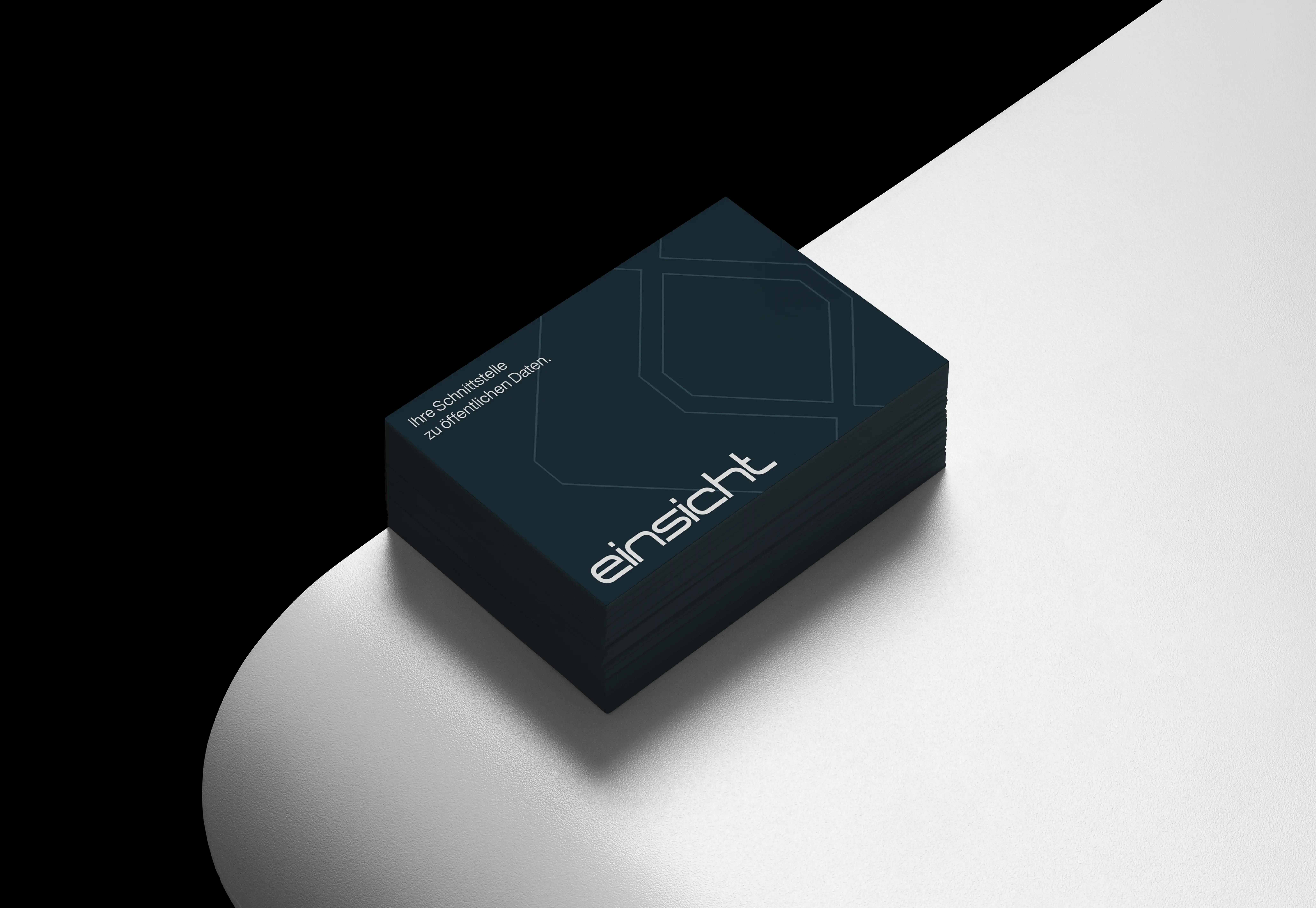 IA-Studio – Branding, Logo Design & Webdesign in Wien Stapel dunkelblauer Visitenkarten der Verrechnungsstelle „einsicht“ mit geometrischem Linienmuster und dem Slogan „Ihre Schnittstelle zu öffentlichen Daten“, präsentiert auf heller, geschwungener Oberfläche.
