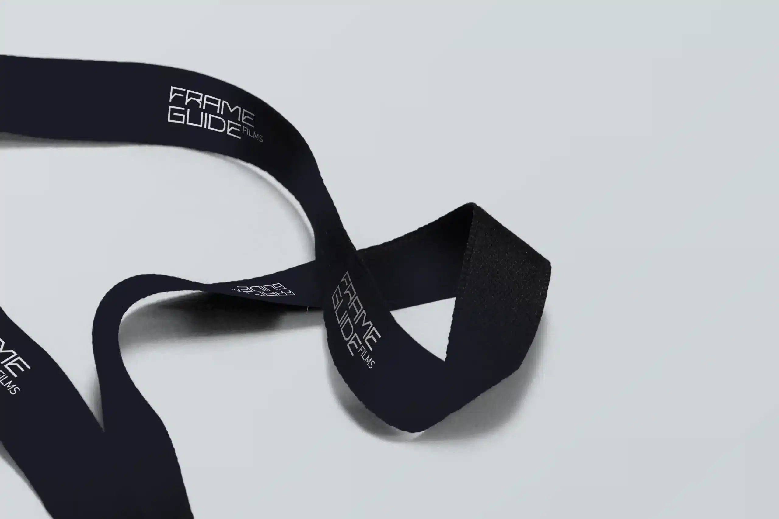 Schwarzes Lanyard mit dem Logo von Frameguide Films auf hellem Hintergrund.